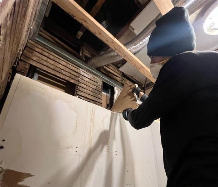 Technician removing damaged drywall, exposed ceiling joists above